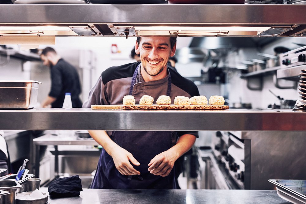 Executive Chef Alex Lepesis in chef whites standing in the restaurant kitchen, showcasing the culinary expertise behind Grandma's modern Greek cuisine